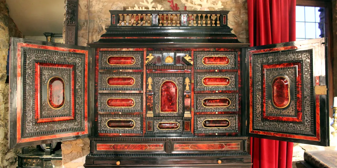 Cabinet anversois du XVIIe siècle en placage d’ébène enrichi de médaillons en écaille de tortue sur fond rouge qui sont encadrés de rinceaux d’argent repoussé ainsi que d’éléments en bronze doré qui enrichissent ce meuble d’apparat présenté ouvert, les vantaux laissant apparaître les nombreux tiroirs.