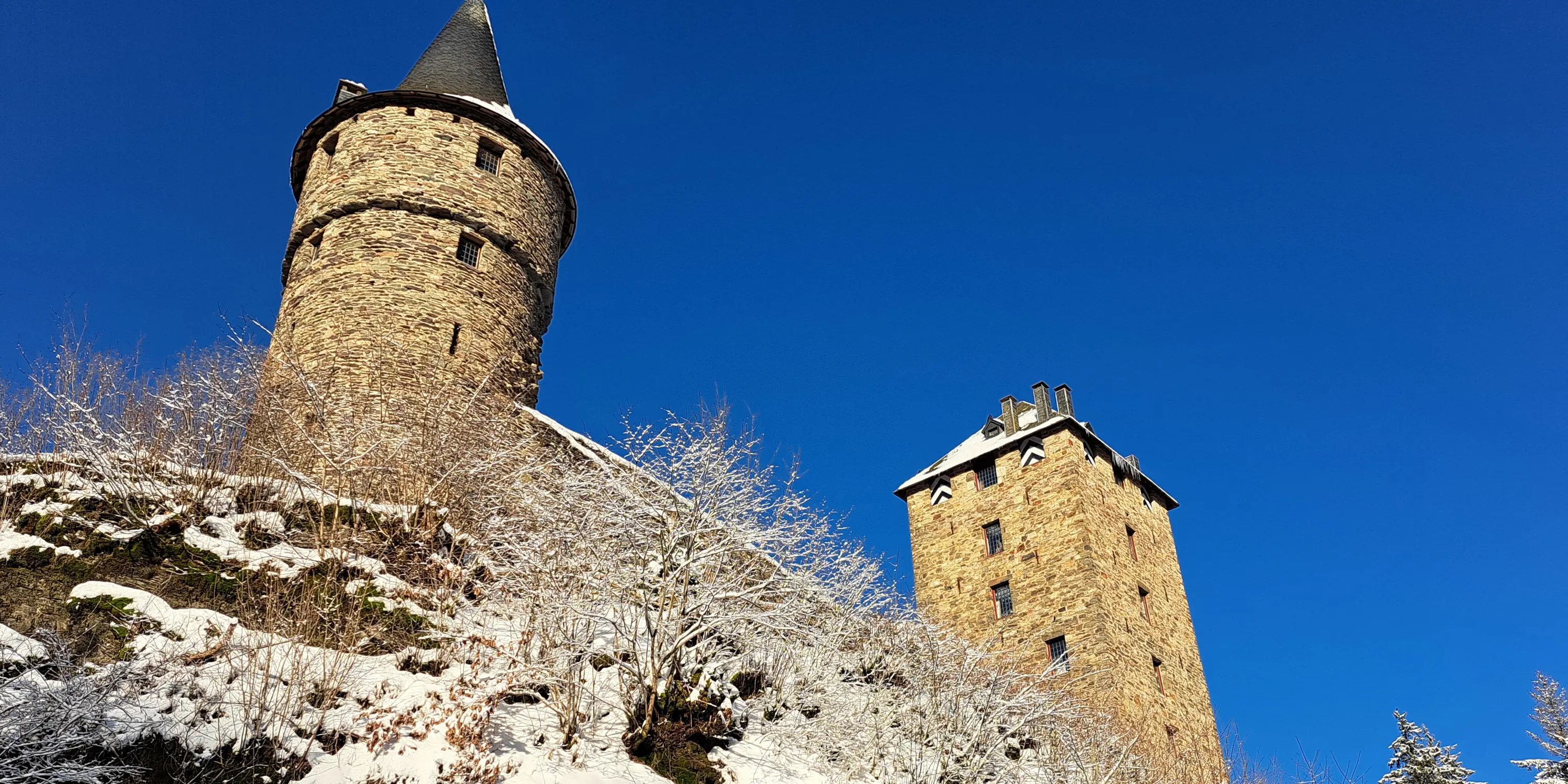 Vue en contre-plongée du château de Reinharstein en hiver, perché au sommet de l’à-pic de 60 mètres qui le protège au Sud et à l’Ouest, avec la tour Salamandre à gauche et le donjon à droite.