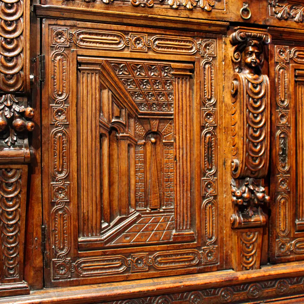 Meuble exposé dans la salle à manger du château de Reinhardstein, ce deux-corps bourguignon en noyer de la seconde moitié du XVIe siècle, de style Renaissance française influencé par Hugues Sambin, offre un décor en perspective architecturale sur les portes, dit en trompe-l'œil ou prospettiva en italien, représentant un intérieur classique avec colonnes, arche, plafond à caissons et sol carrelé.