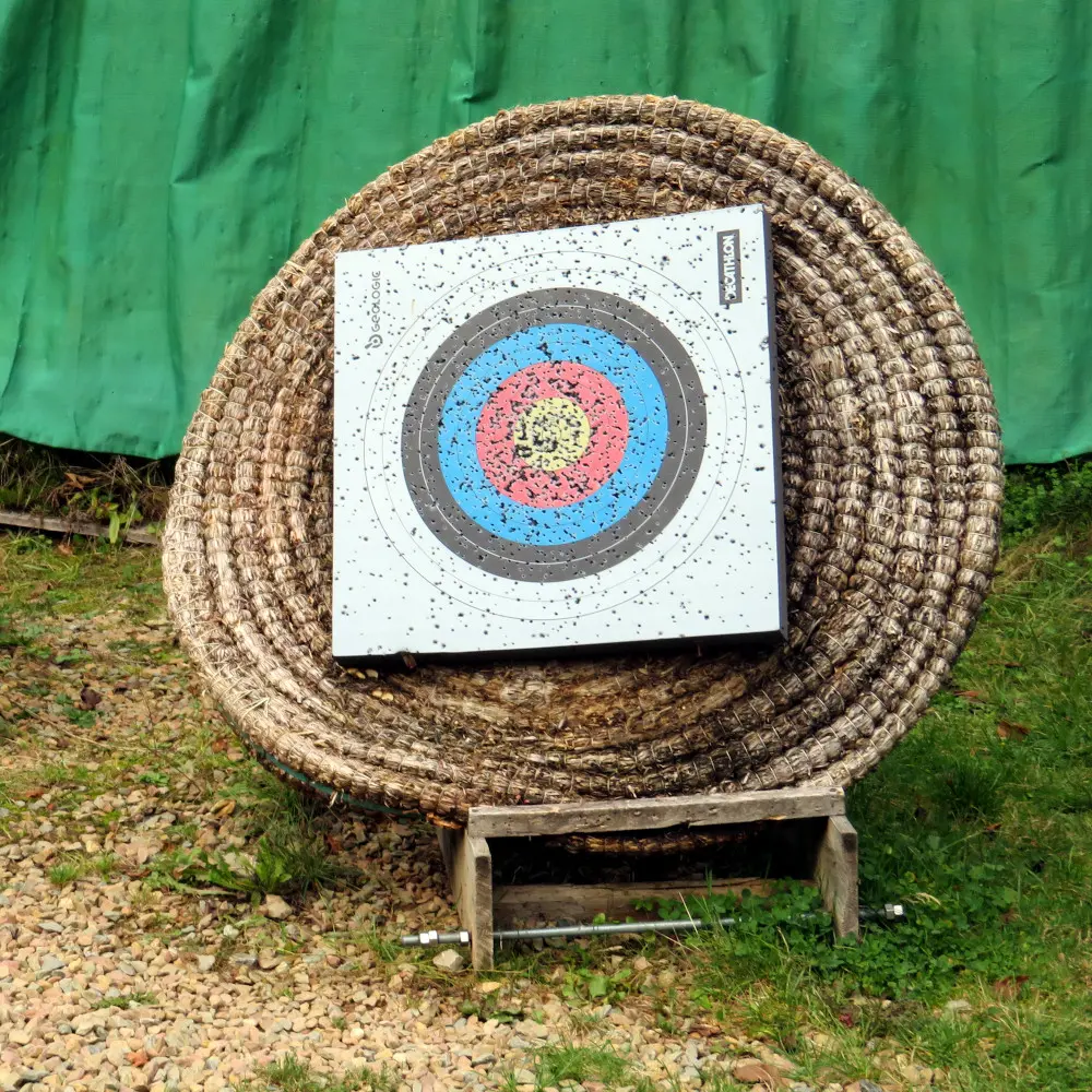 Cible de tir à l'arc classique de type FITA, fixée sur un support en paille tressée portant des marques d’impacts de flèches, posée sur un socle en bois rustique dans la cour du château de Reinhardstein.