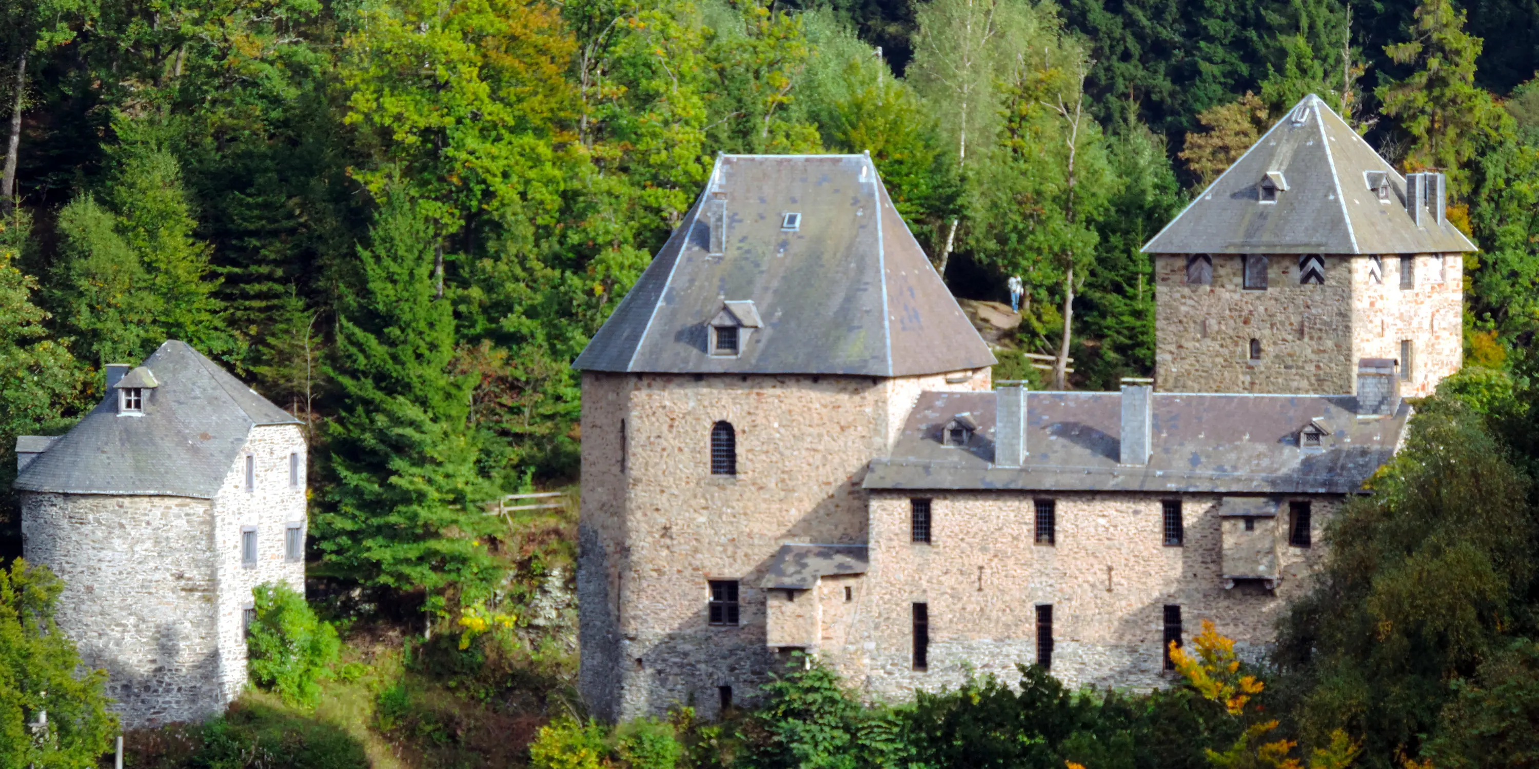 Vue du château de Reinhardstein prise depuis l’Ouest montrant l’étagement des vieilles toitures d’ardoise d’où émergent des lucarnes et des souches de cheminées.